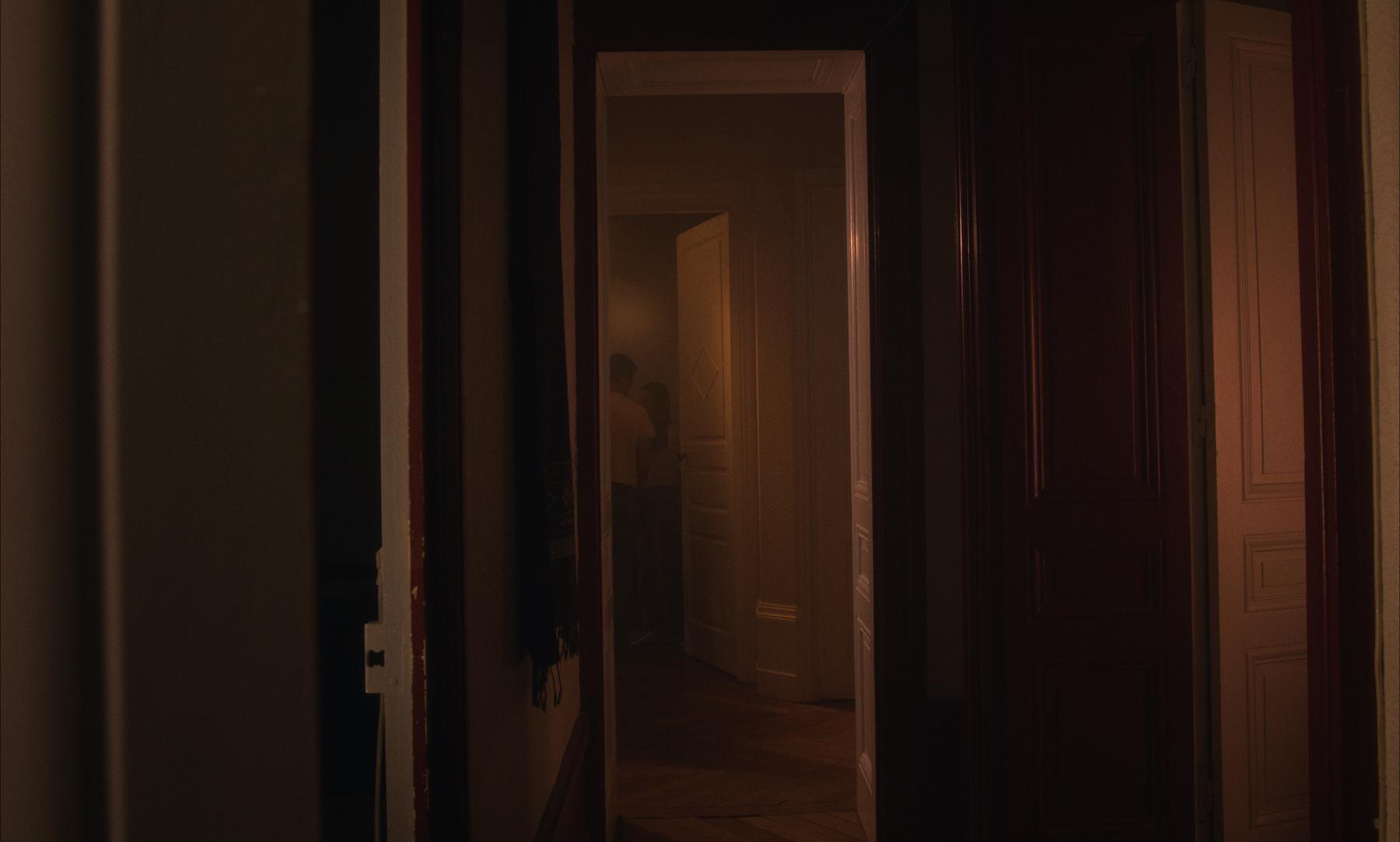 Photogramme : un couloir sombre, un couple entrevu au fond de l'appartement.