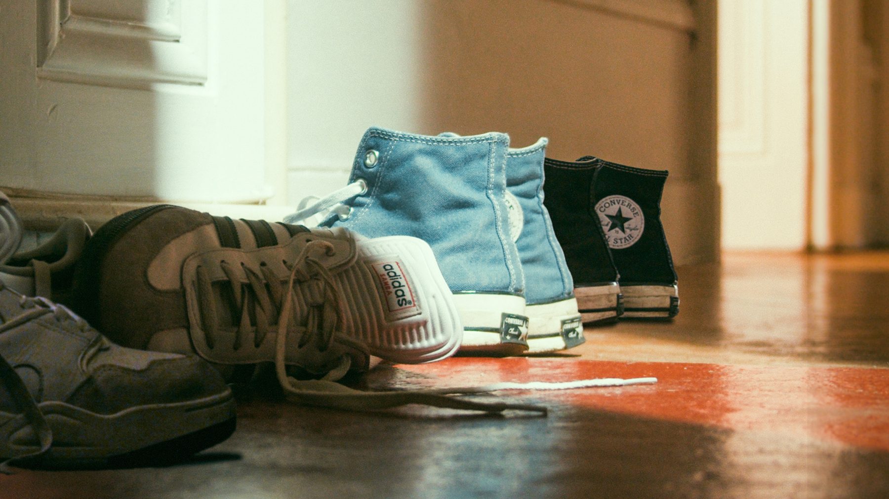 Photogramme d'Un Ange Aimé : des paires de chaussures alignées dans l'entrée d'un appartement, lumière chaude.