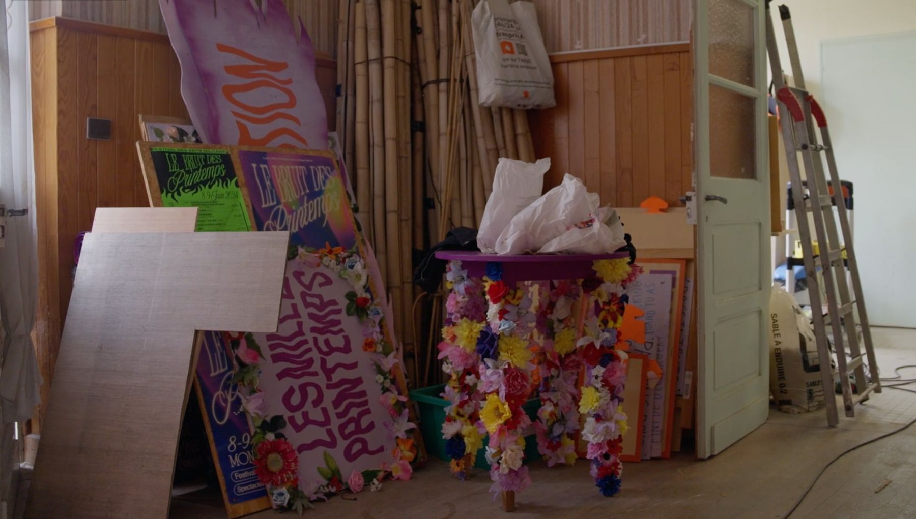 Tournage de Lieu Dire : la réserve du festival — pancartes peintes du Bruit des Printemps, table fleurie et bambous.