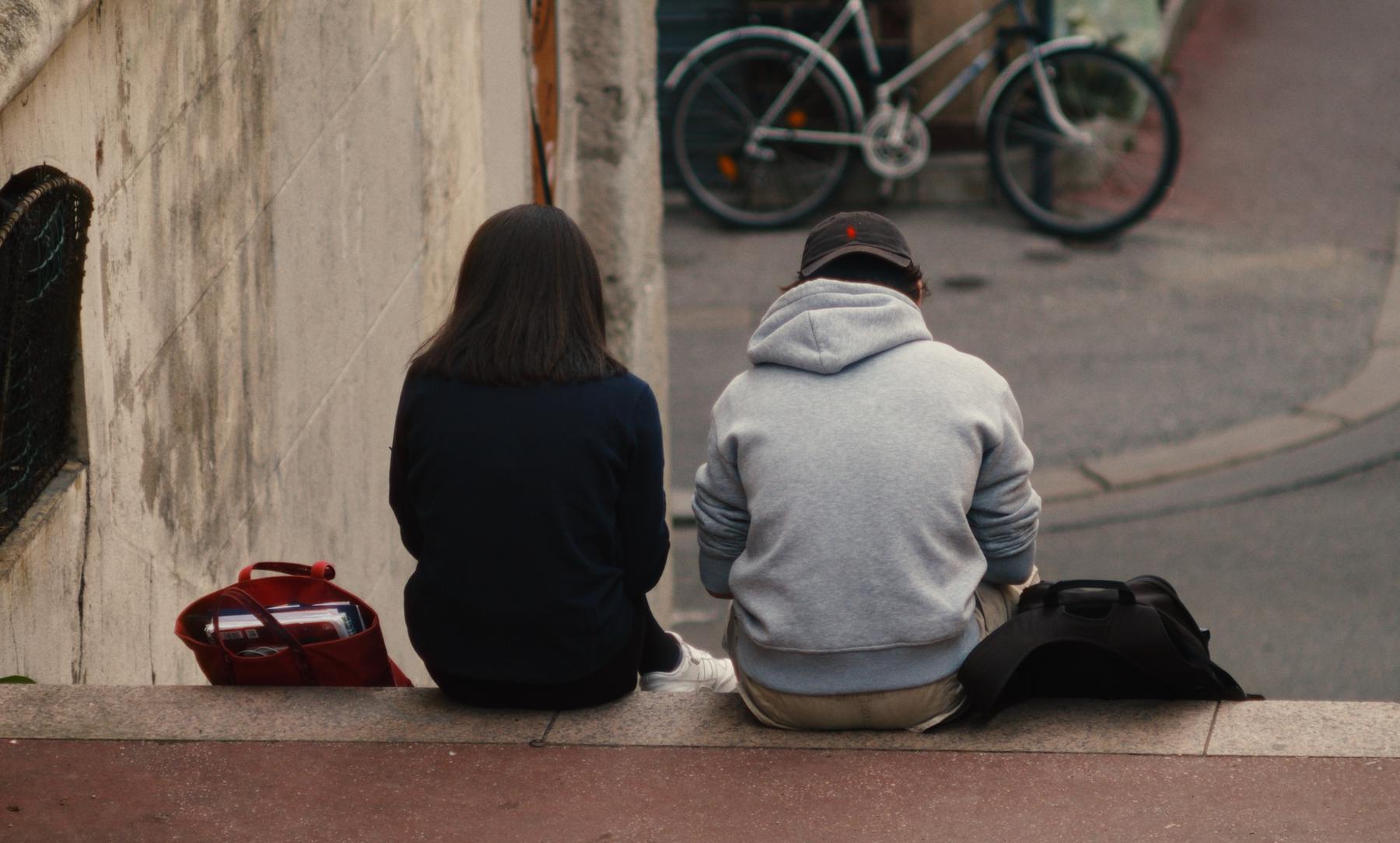 Photogramme : un couple assis de dos en haut d'un escalier, un vélo blanc en contrebas.