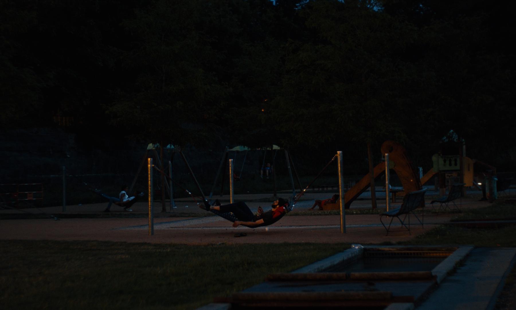 Photogramme : un homme allongé dans un hamac d'aire de jeux, à la tombée de la nuit.